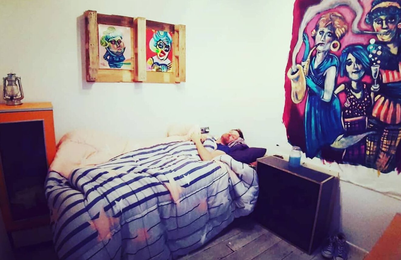 Uli Pforr schlafend im Bett unter eigenen Bildern.