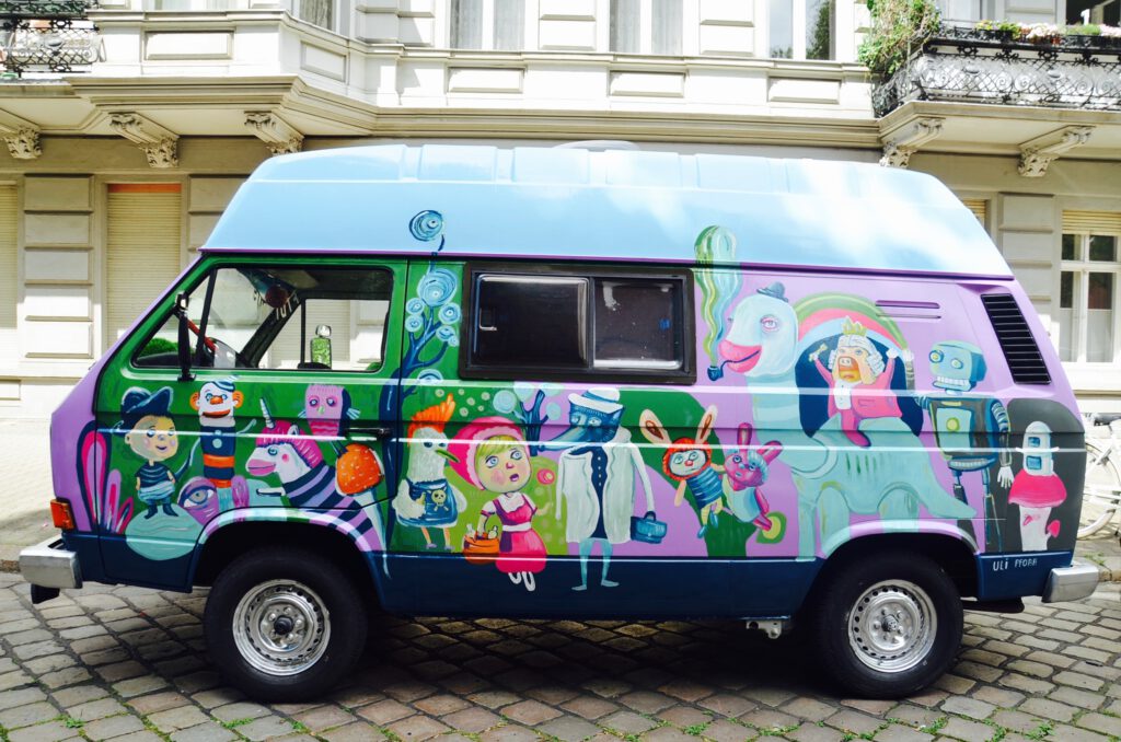 Von Uli Pforr bemalter T3 Bus mit blauem Dach vor Altbau. Mit märchenhaften Figuren und Pflanzen bemalt.